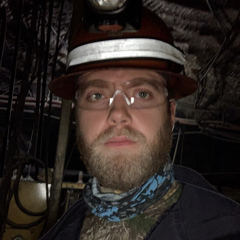 Dan Gauerke underground, cap lamp on, cable runs and ground support behind him