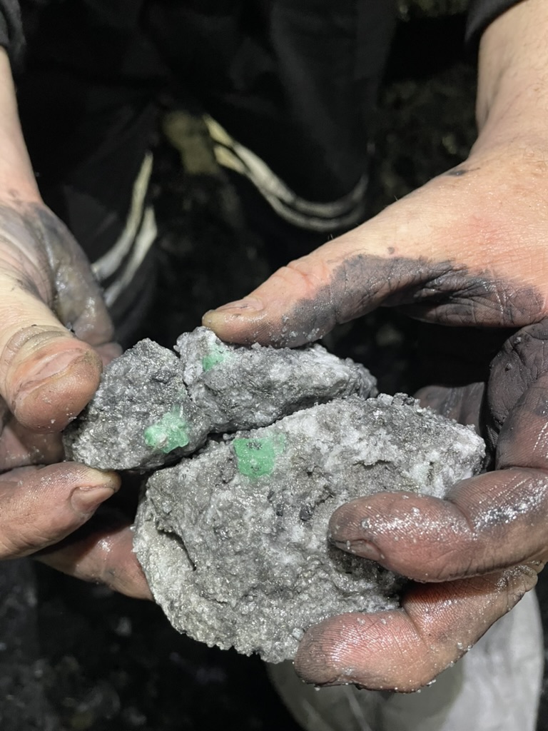A miner's hands holding emeralds in the host rock