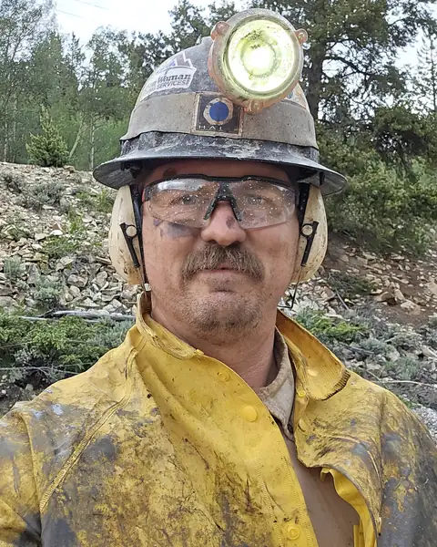 Ben Litsey in yellow rain gear, hard hat, cap lamp, safety glasses and ear muffs